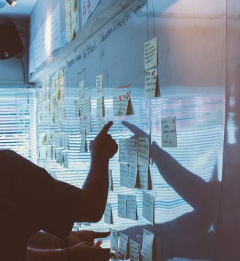 Eine Person steht vor einem Whiteboard, an dem mehrere Post-its kleben.