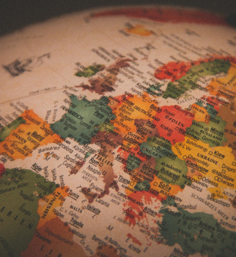 Ein Globus in warmer Beleuchtung zeigt einen detaillierten Ausschnitt von Europa und Teilen Nordafrikas. Die Länder sind in verschiedenen Farben markiert, mit gut lesbaren Städtenamen und geografischen Bezeichnungen. Deutschland, Frankreich, Italien und die angrenzenden Staaten sind zentral im Bild, während das Bild nach oben hin unscharf wird. Der Druckstil erinnert an einen klassischen Schulglobus.