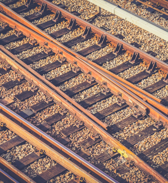 Mehrere rostbraune Eisenbahnschienen auf Holzschwellen im Schotter