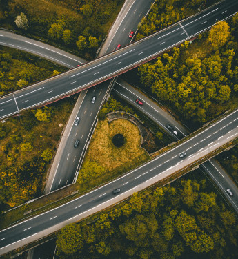 Mehrspuriges Autobahnkreuz mit mehreren Autos, umgeben von dichtem grün-gelbem Wald.