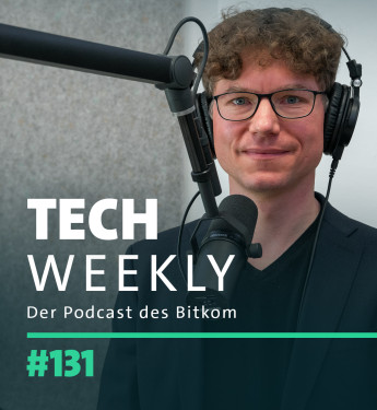 Mann mit lockigem, braunem Haar in schwarzem Sakko vor Mikrofon und Kopfhörern. Hintergrund in Grautönen.