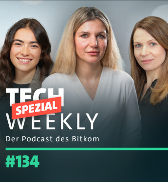 Drei Frauen stehen nebeneinander, jede in unterschiedlichen Oberteilen. Hintergrund unscharf, Text in der linken unteren Ecke.