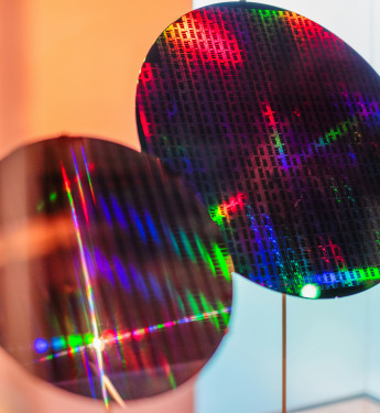 Zwei runde Siliziumwafer in einer Vitrine, reflektieren buntes Licht, mit orangefarbener Beleuchtung im Hintergrund.