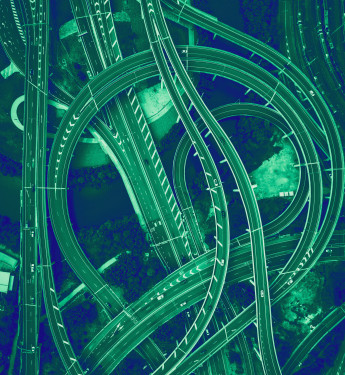 Luftaufnahme eines Autobahnkreuzes mit Über- und Unterführungen, weißen Fahrtrichtungs-Pfeilen und grüner Vegetation.