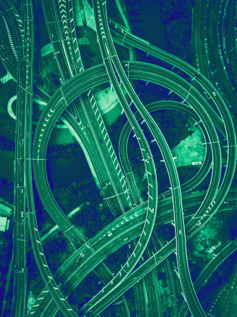 Luftaufnahme eines Autobahnkreuzes mit Über- und Unterführungen, weißen Fahrtrichtungs-Pfeilen und grüner Vegetation.