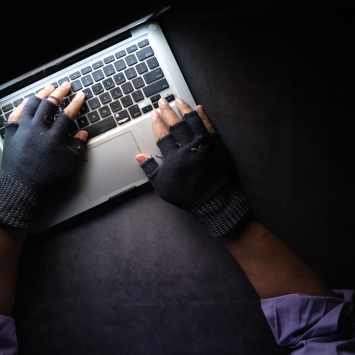  Hände in fingerlosen Handschuhen tippen am Laptop, dunkle Atmosphäre 