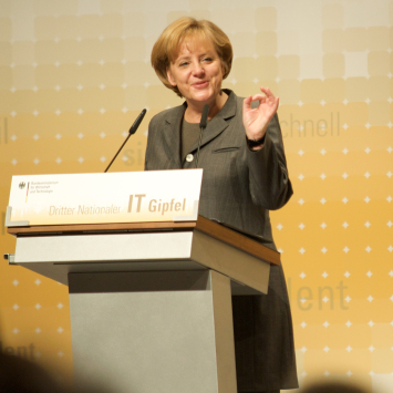 Merkel steht hinter einem Rednerpult, lächelt und hält eine Rede.