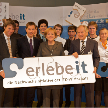 U.a. Scheer, Berg und Merkel halten ein Schild mit der Aufschrift "Erlebe IT - eine Nachwuchsinitiative der ITK-Wirtschaft.