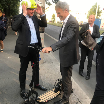 Andreas Scheuer erscheint mit einem E-Roller zum Sommerfest, Achim Berg begrüßt ihn.