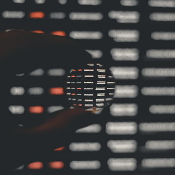 Eine Hand hält eine Linse vor einen unscharfen Datenbildschirm.