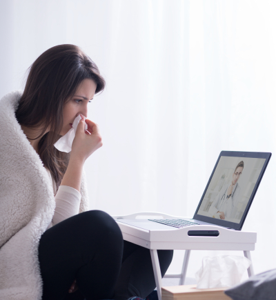 Frau sitzt vor Laptop und putzt sich die Nase