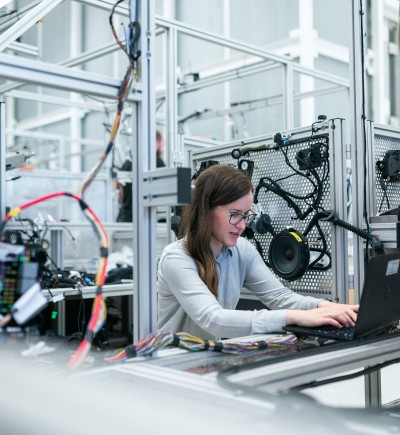 Frau sitzt in Industriewerkstatt am Laptop