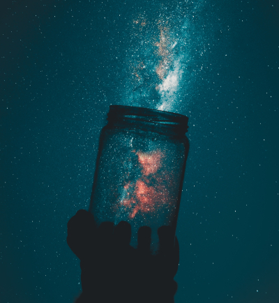 Hand hält Glas vor Hintergrund des Nachthimmels