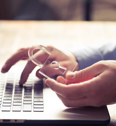 Am Laptop arbeitende Hände, eine Hand hält Glasschloss