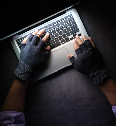  Hände in fingerlosen Handschuhen tippen am Laptop, dunkle Atmosphäre 