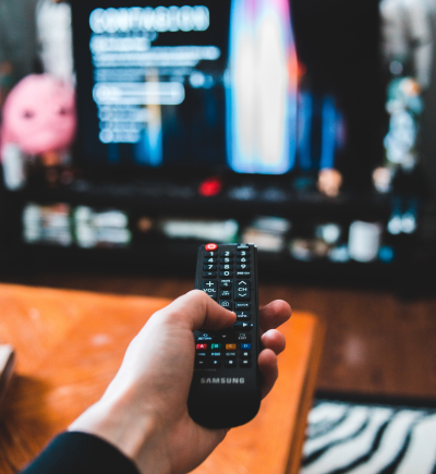 Person sitzt mit Fernbedienung vor einem Fernseher