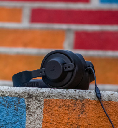 Ein schwarzer, kabelgebundener Kopfhörer liegt auf einer Betonmauer, die in blauen, orangen und grünen Rechtecken bemalt ist.