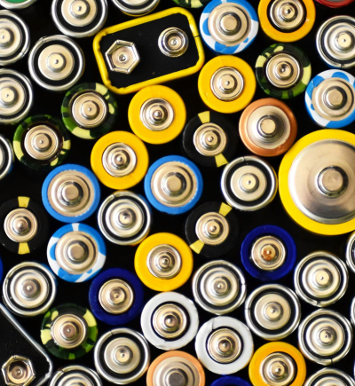 Dicht angeordnete Batterien in verschiedenen Größen und Farben, von oben auf ihre Pole fotografiert.
