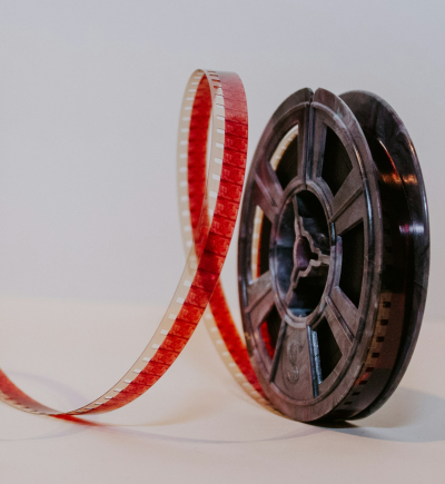 Schwarze Filmrolle mit locker geschwungenem roten 35-mm-Filmstreifen auf hellem Hintergrund.