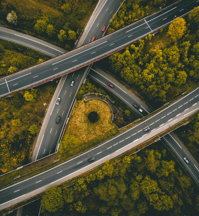 Mehrspuriges Autobahnkreuz mit mehreren Autos, umgeben von dichtem grün-gelbem Wald.