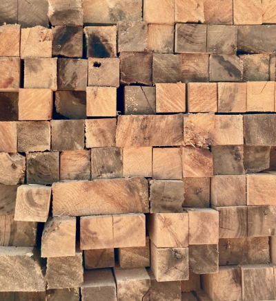 Unbehandelte, quadratische Holzbalken liegen gestapelt mit sichtbaren Maserungen.