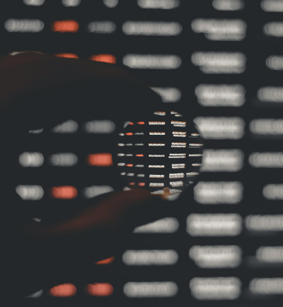 Eine Hand hält eine Linse vor einen unscharfen Datenbildschirm.