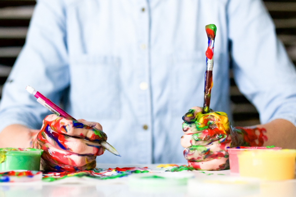 Mensch sitzt mit Pinseln und Farbe am Tisch und malt