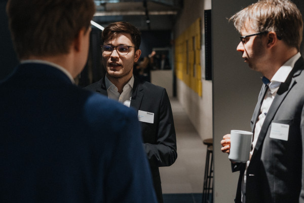 Impression vom Eingang des AI Infrastructure Day, drei Männer in Anzügen unterhalten sich.