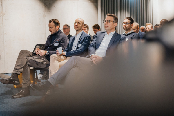 Impression der ersten Reihe beim AI Infrastructure Day, drei Männer in Anzügen hören aufmerksam zu.