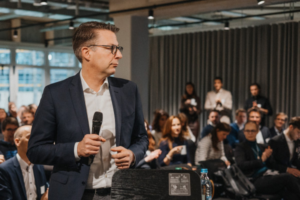 Markus Blume, Staatsminister, in Anzug und mit Mikrofon in der Hand, bereitet sich vor, bei AI Infrastructure Day zu sprechen.