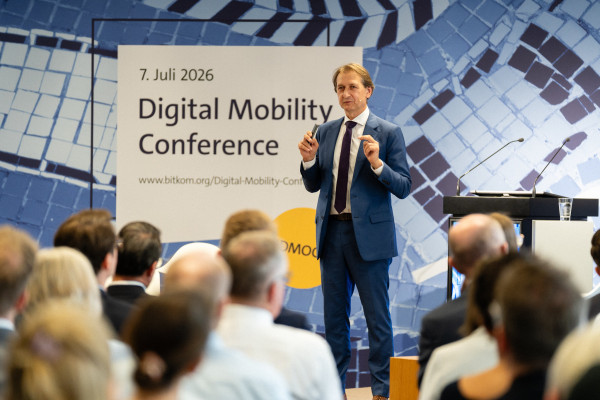 Mann in blauem Anzug spricht auf Bühne, Banner „7. Juli 2026 Digital Mobility Conference“ im Hintergrund.