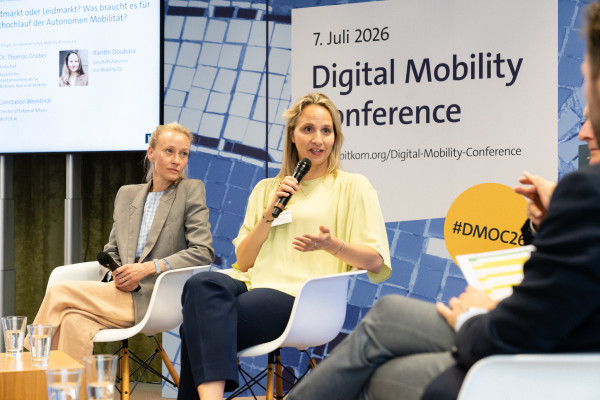 Zwei Personen diskutieren auf Stühlen, ein Banner mit „7. Juli 2026 Digital Mobility Conference“ im Hintergrund.